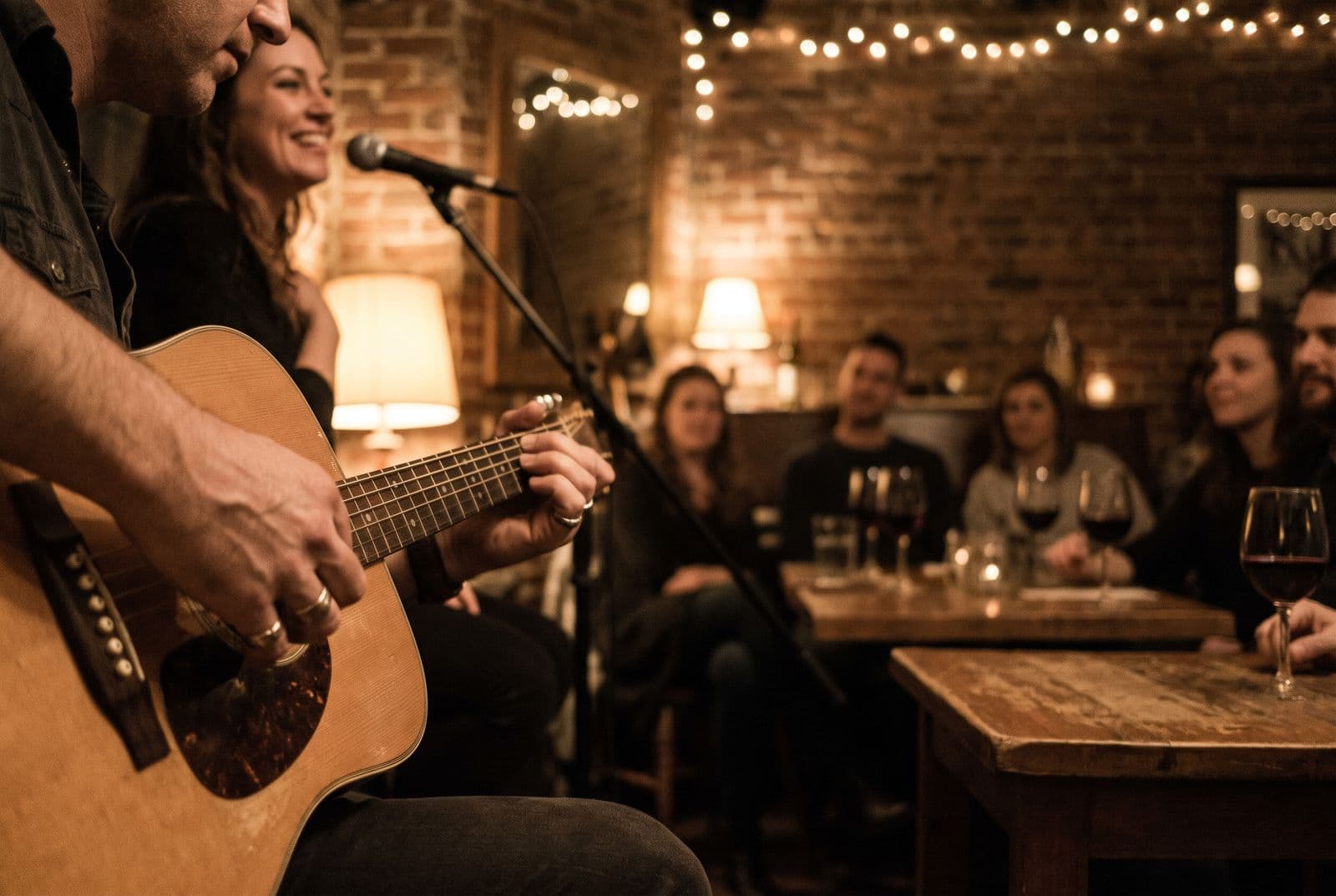 Close up of hands on an acoustic guitar as a duo sings to a small wine bar crowd.